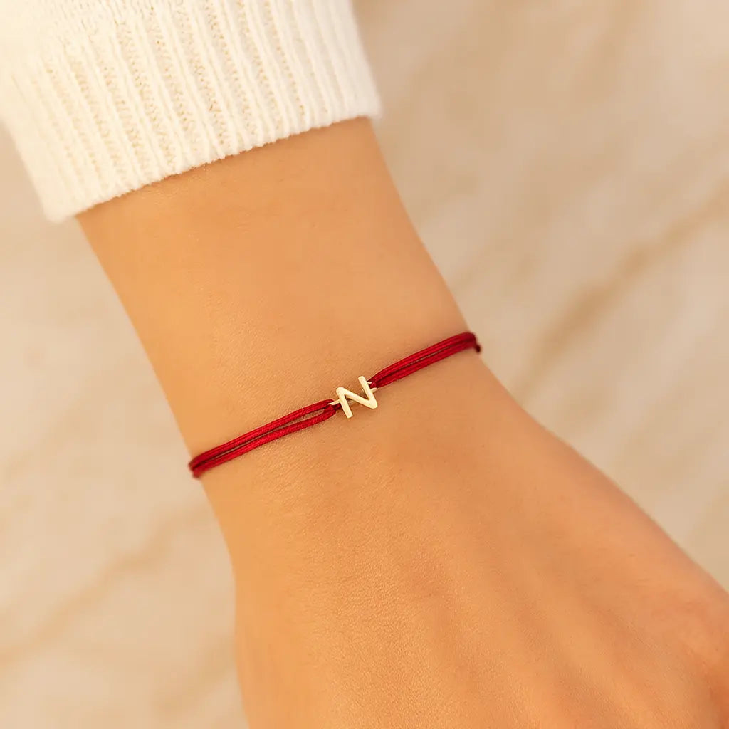 Red bracelet with a gold charm on a wrist against a beige background