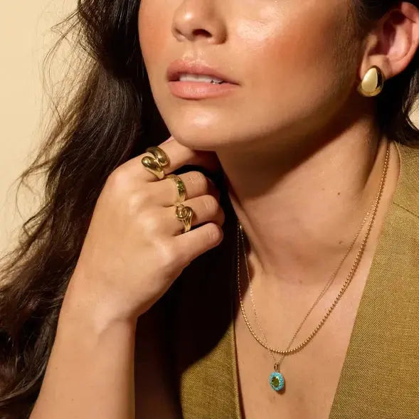 Close-up of a woman wearing gold jewelry including earrings, rings, and a necklace.
