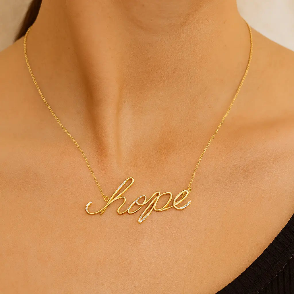 Gold necklace with 'hope' pendant on a person wearing a black top.