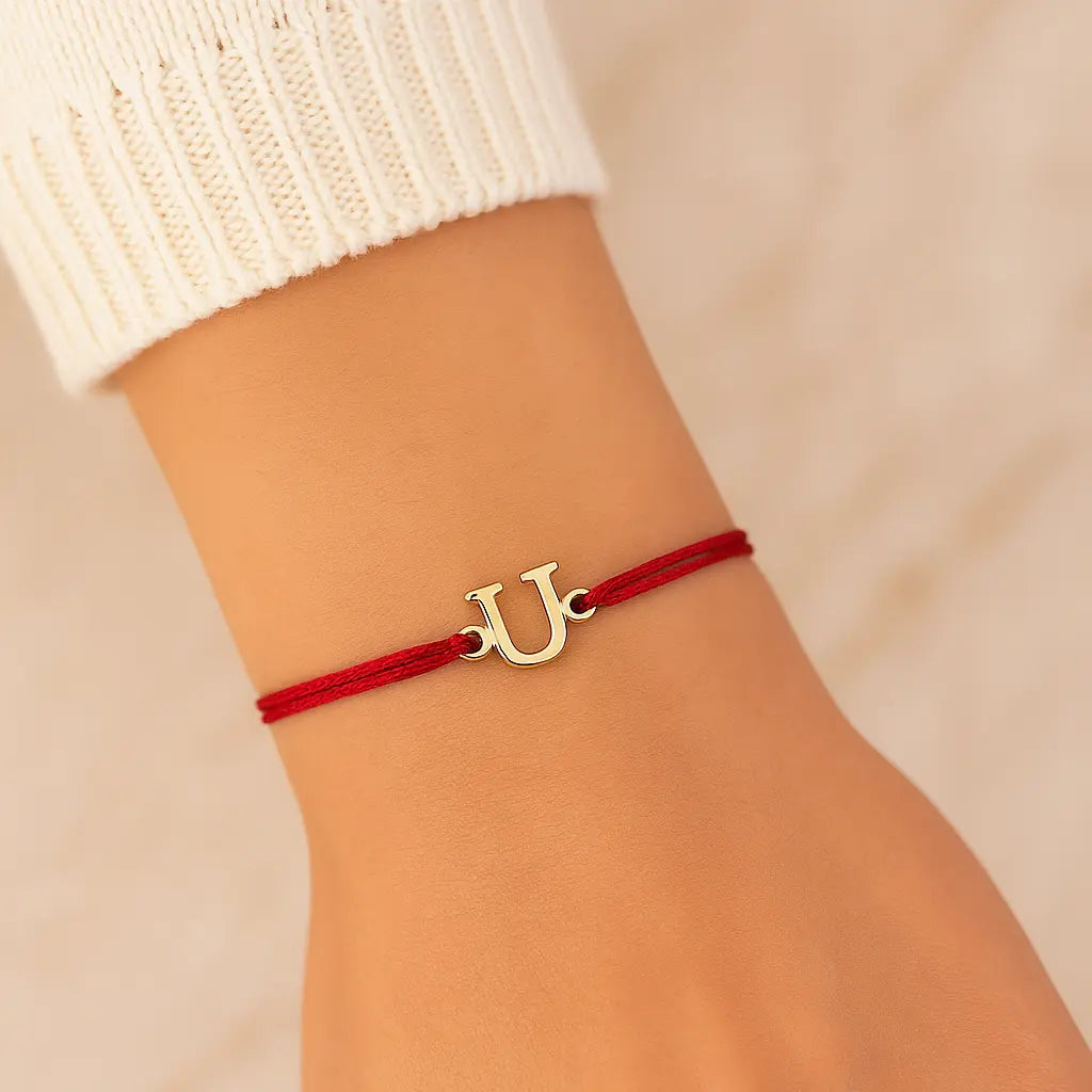 Red bracelet with a gold 'U' charm on a wrist against a beige background