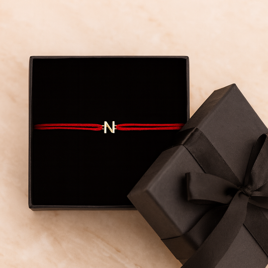 Black gift box with red ribbon and 'N' logo on a beige surface